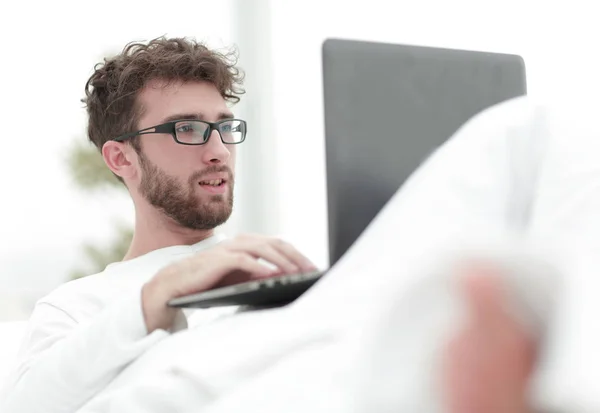 Smiling man using laptop lying on bed — Stock Photo, Image