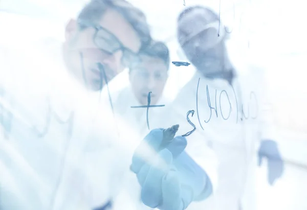 Close up.a group of scientists recording the formula on a glass — Stock Photo, Image