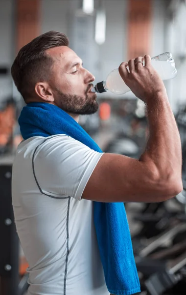 Молодой мужчина пьет бутылку воды на беговой дорожке в спортзале . — стоковое фото