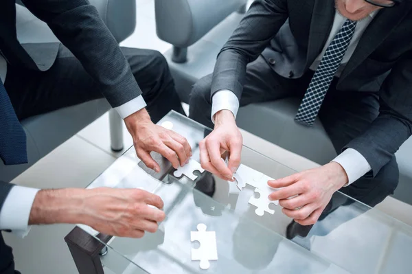 Close up.business partners putting together a puzzle, sitting at office Desk — стоковое фото