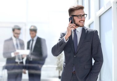 Banka ofisinin yanında cep telefonu olan bir işadamı duruyor.