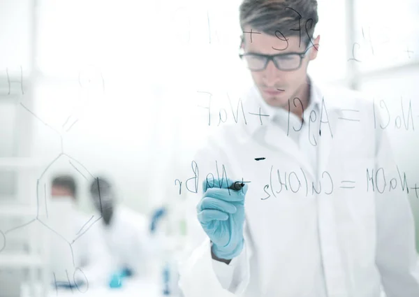 Serious scientist writes a chemical formula on a glass Board. — Stock Photo, Image