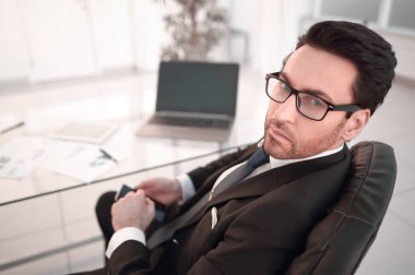 Masasında oturan ve kameraya bakarak işadamı