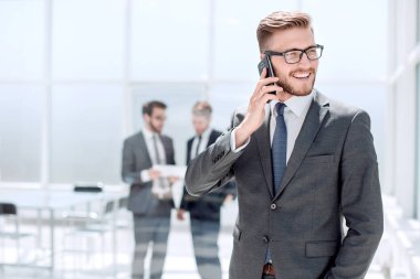 Banka ofisinin yanında cep telefonu olan bir işadamı duruyor.
