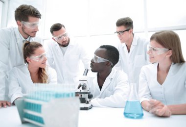 Odaklanmış ve ciddi kadın ve erkek kimyagerler laboratuvar önlükleri ve güvenlik gözlükleri takıp deneyler yapıyorlar.