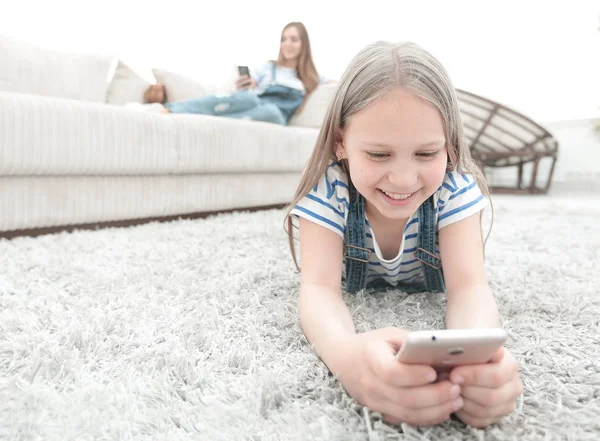 stock image cute little girl with smartphone lying on the carpet in the living room