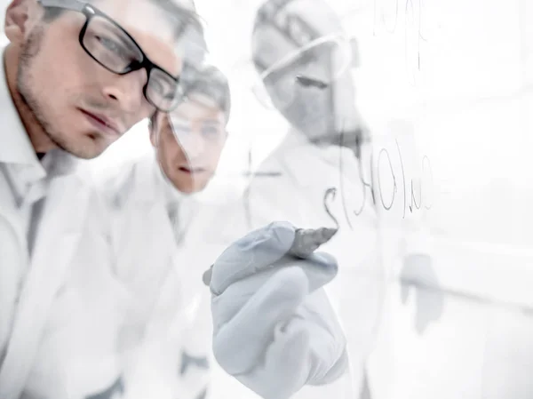 Close up. Un gruppo di scienziati che registra la formula su una lavagna di vetro . — Foto Stock