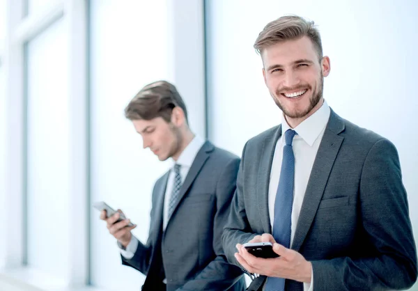 Empleados exitosos usando sus teléfonos inteligentes sentados en el vestíbulo de la oficina — Foto de Stock