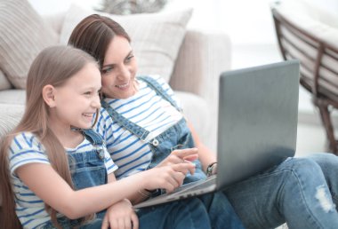 Anne ve kızı oturma odasında halıya oturmuş dizüstü bilgisayar kullanıyorlar.