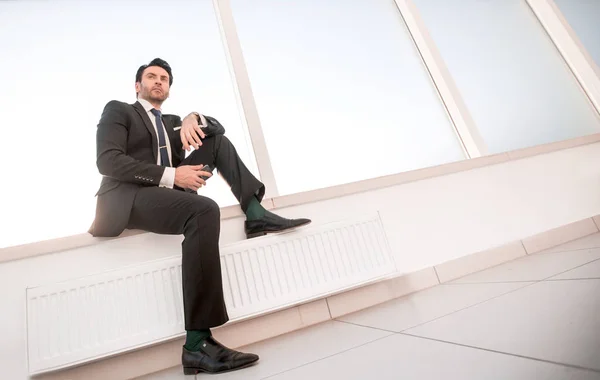 Уверенный в себе бизнесмен со смартфоном, сидящим в коридоре офиса — стоковое фото