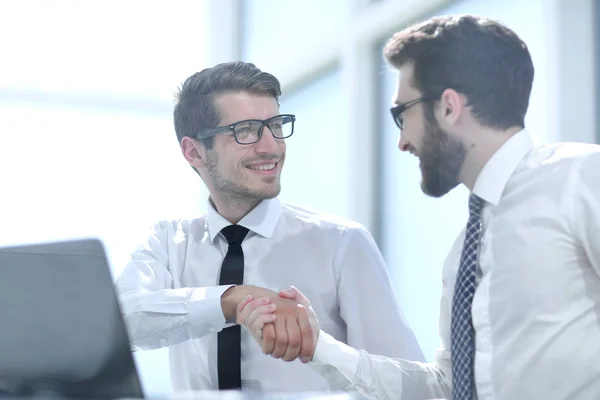 Handshake współpracownikami siedzi przy biurku — Zdjęcie stockowe