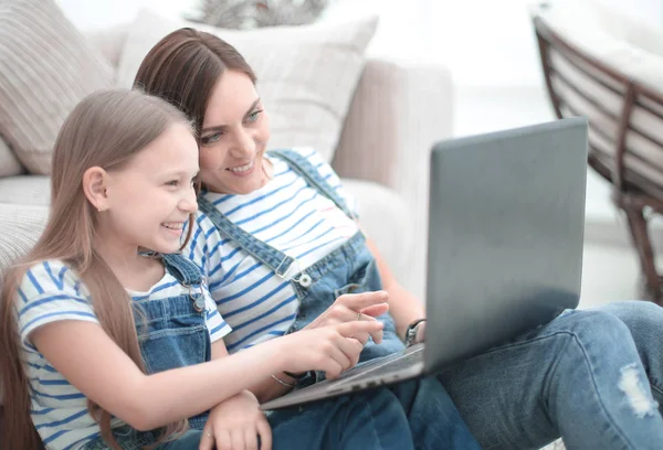Moeder en dochter zitten op het tapijt in de woonkamer en met behulp van een laptop — Stockfoto