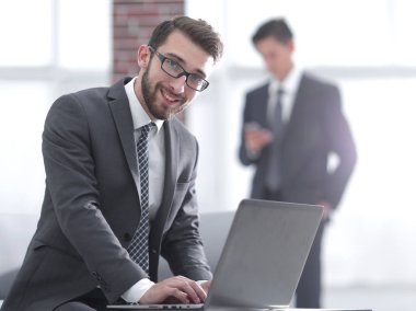 Yakışıklı iş adamı ofiste dizüstü bilgisayarla çalışıyor.