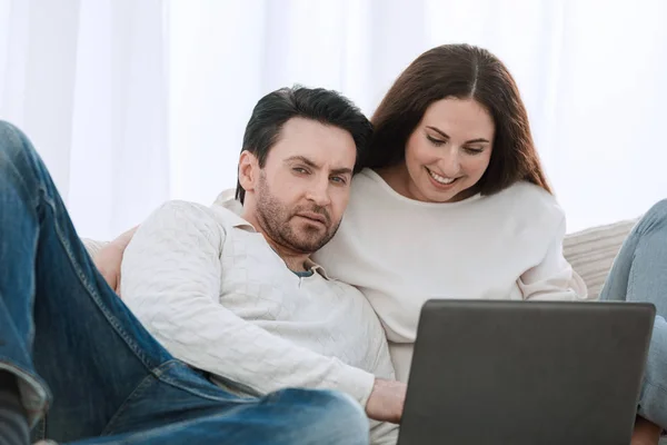 Feliz casal sentado no sofá em seus braços, olhando para laptop — Fotografia de Stock