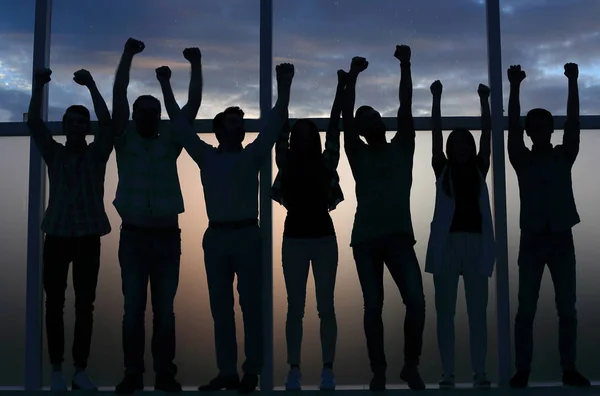 business team standing near the window with hands up