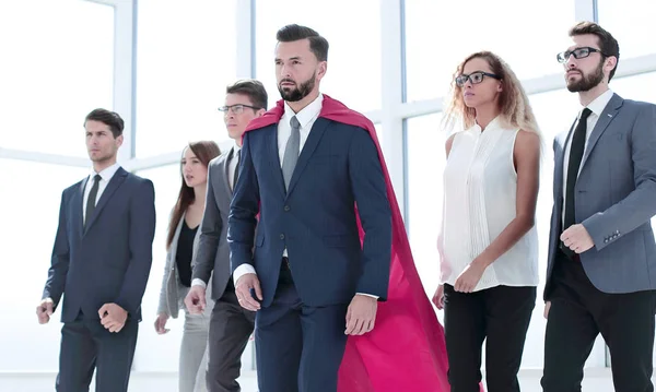 Homem de negócios em Superman capa e equipe de negócios de pé no lobby do escritório — Fotografia de Stock