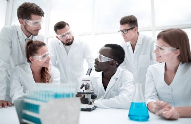 Odaklanmış ve ciddi kadın ve erkek kimyagerler laboratuvar önlükleri ve güvenlik gözlükleri takıp deneyler yapıyorlar.