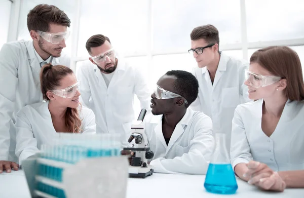 Сосредоточенные и серьезные химики-женщины и мужчины в лабораторных халатах и защитных очках проводят эксперименты — стоковое фото