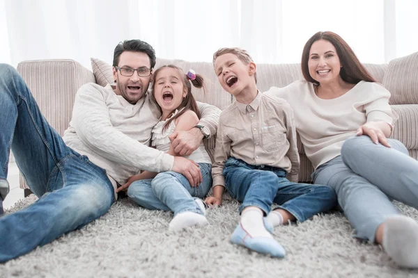 Lycklig familj sitter på mattan i vardagsrummet — Stockfoto