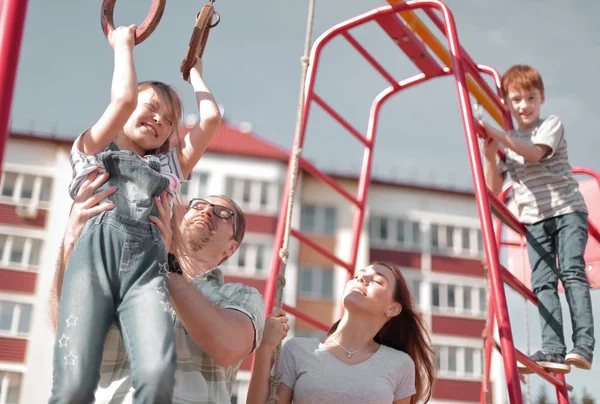 Ung familj med barn som leker på lekplatsen — Stockfoto