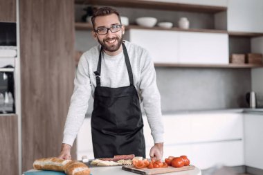 Önlüklü bir adam sandviçler için salam kesiyor.
