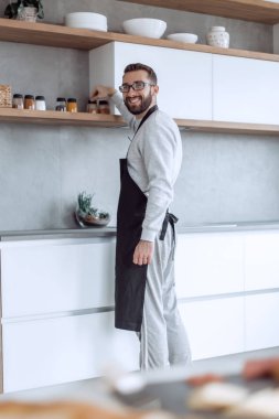 Gülümseyen adam mutfakta baharat seçiyor.