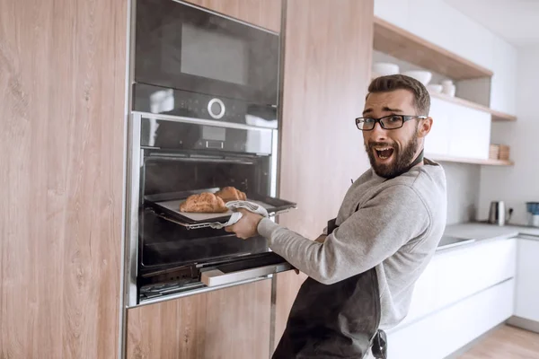 Close up. a young man takes out of the oven tray of croissants — Stock Photo, Image