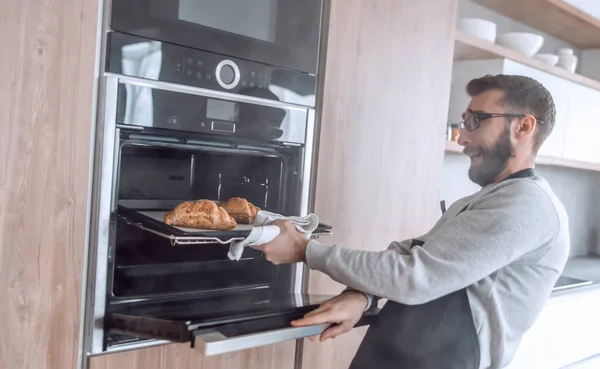 De cerca. un joven saca de la bandeja del horno de croissants — Foto de Stock