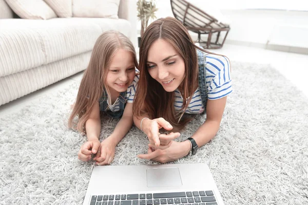 Anya és lánya feküdt a szőnyegen, és használ egy laptop — Stock Fotó