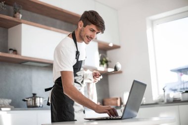 Genç adam yemek pişirirken dizüstü bilgisayara bakıyor.