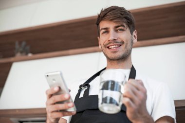 Mutfakta bir smartphone ayakta ile gülümseyen genç adam.
