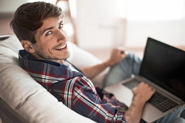 Vista laterale. giovane uomo di successo con computer portatile seduto sulla sedia — Foto Stock