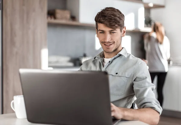 Jonge man werkt online zittend aan keuken tafel — Stockfoto