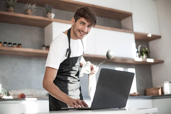 Молодой человек смотрит на экран ноутбука во время приготовления ужина — стоковое фото