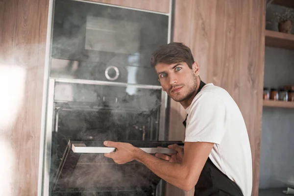 Frustrated young man standing near broken oven — Stock Photo, Image