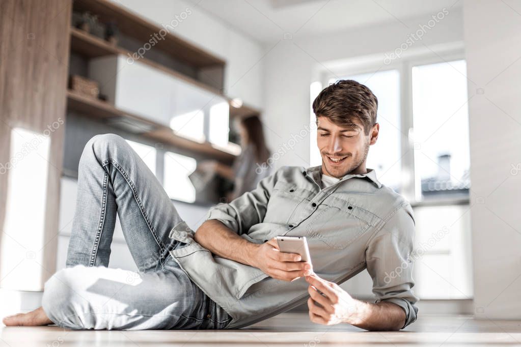 young man with smartphone sitting on kitchen floor