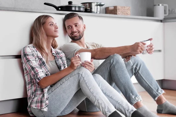 Młoda para pije kawę siedząc na podłodze w kuchni — Zdjęcie stockowe