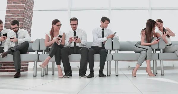 Geschäftskollegen sitzen mit ihren Smartphones in der Lobby des Büros — Stockfoto