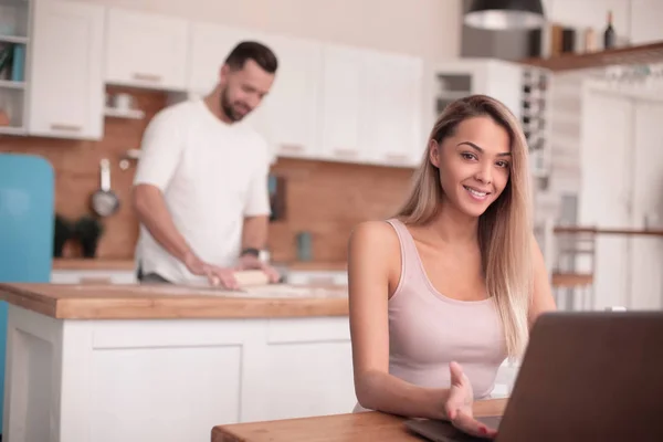 Jovem mulher sentada na frente do laptop aberto na cozinha — Fotografia de Stock