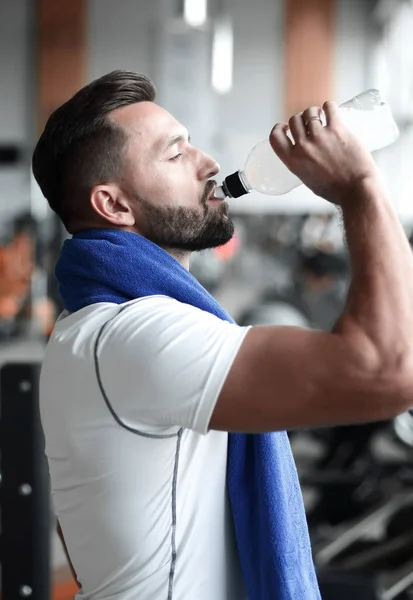 Junger Erwachsener trinkt Wasserflasche auf Laufband in Turnhalle. — Stockfoto