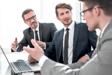 Ofis masasında oturan çalışanlar iş planını tartışıyor.