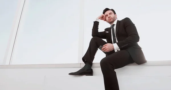 Confident businessman with a smartphone sitting in the office hallway — Stock Photo, Image