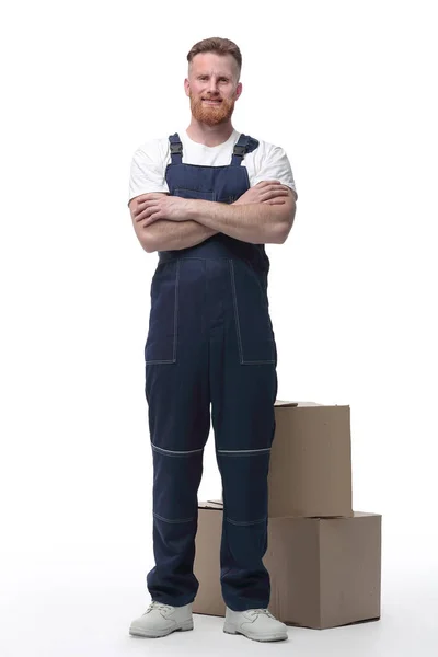 Дружелюбный человек в комбинезоне, стоящий рядом с картонными коробками — стоковое фото