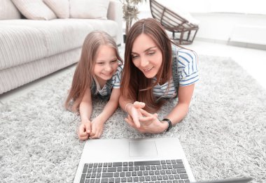 Anne ve kızı halı üzerinde yalan ve bir dizüstü bilgisayar kullanarak