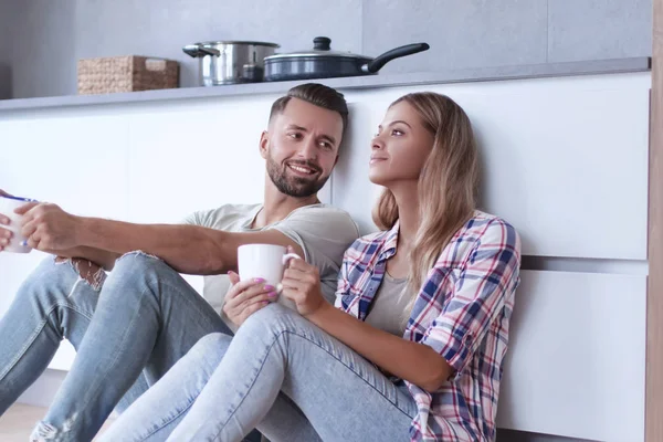 Pareja joven tomando café sentado en el suelo de la cocina — Foto de Stock