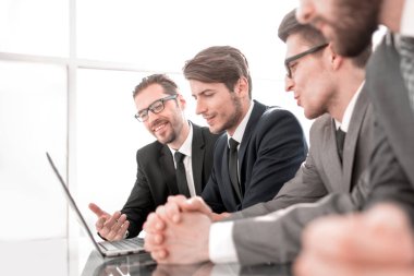 Bir dizüstü bilgisayarın önünde bir masada oturan gülümseyen iş adamları