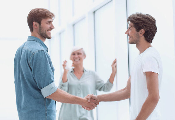 Коллеги пожимают руки в холле офиса
