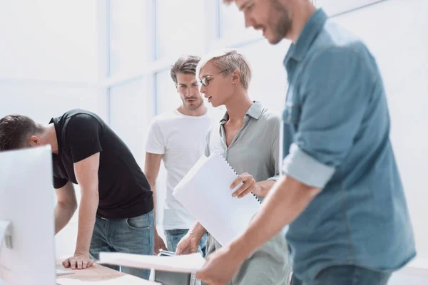 Group of designers with sketches standing near the desktop — Stock Photo, Image