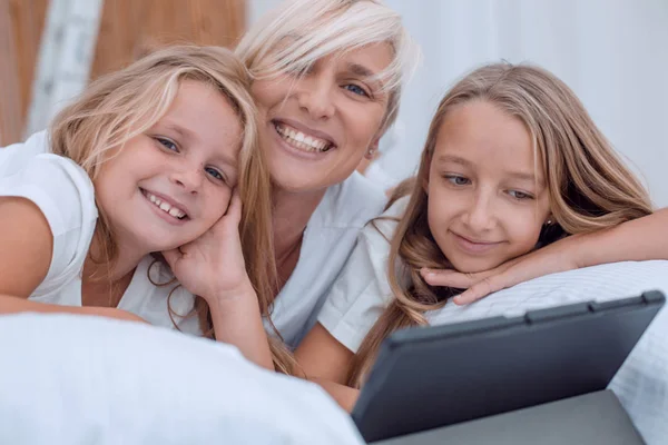 Mãe com suas meninas assistindo vídeos deitado na cama — Fotografia de Stock