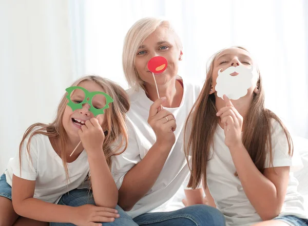 Mãe e suas meninas com máscaras divertidas estão sentadas no sofá . — Fotografia de Stock